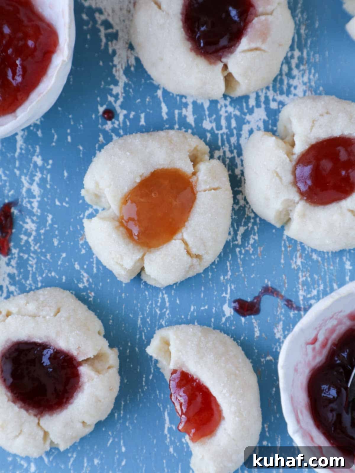 Assortment of vibrant thumbprint cookies with different jam fillings displayed on a blue board.