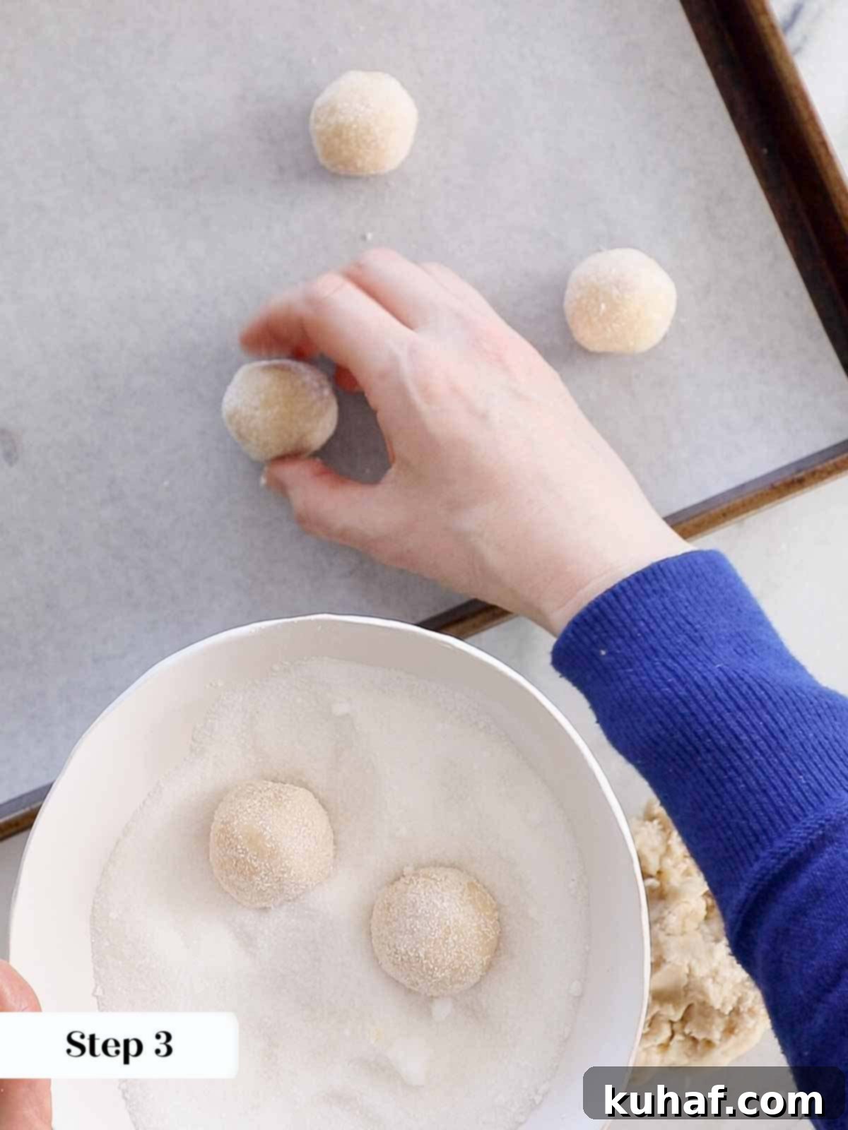 Rolling cookie dough in granulated sugar then placing on a baking sheet.