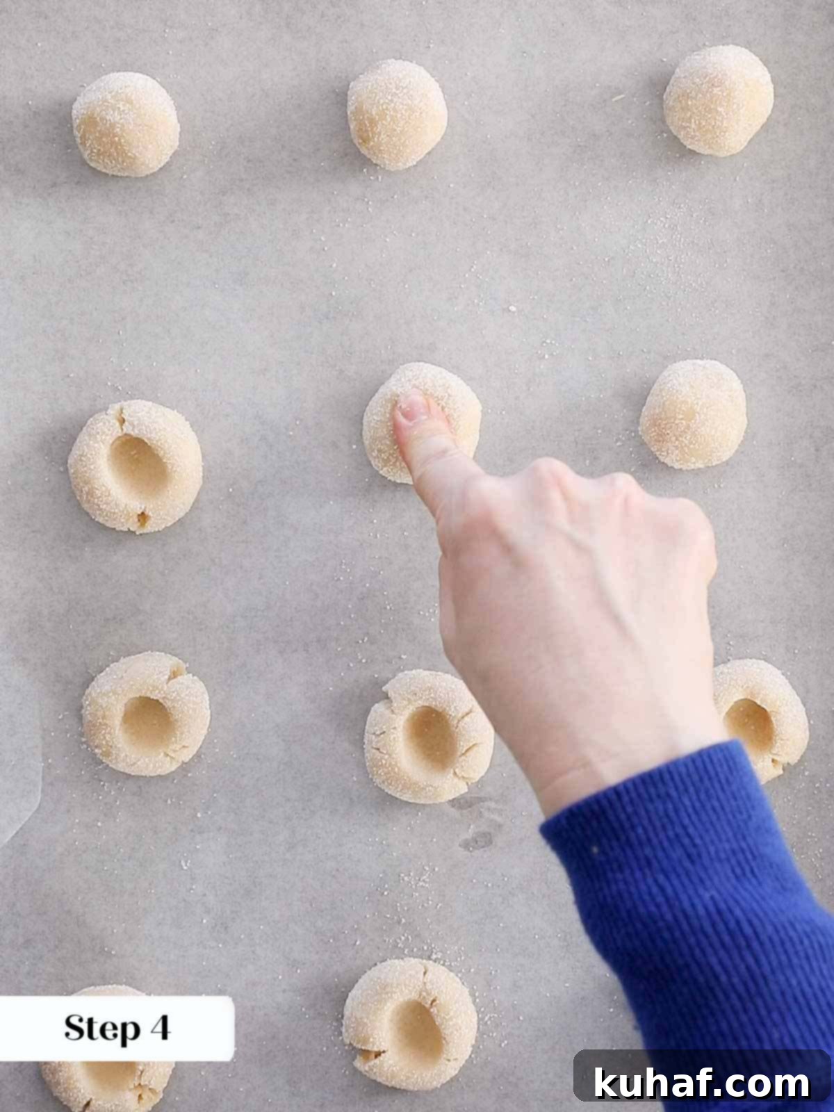 Finger making an indentation in a thumbprint cookie dough ball.
