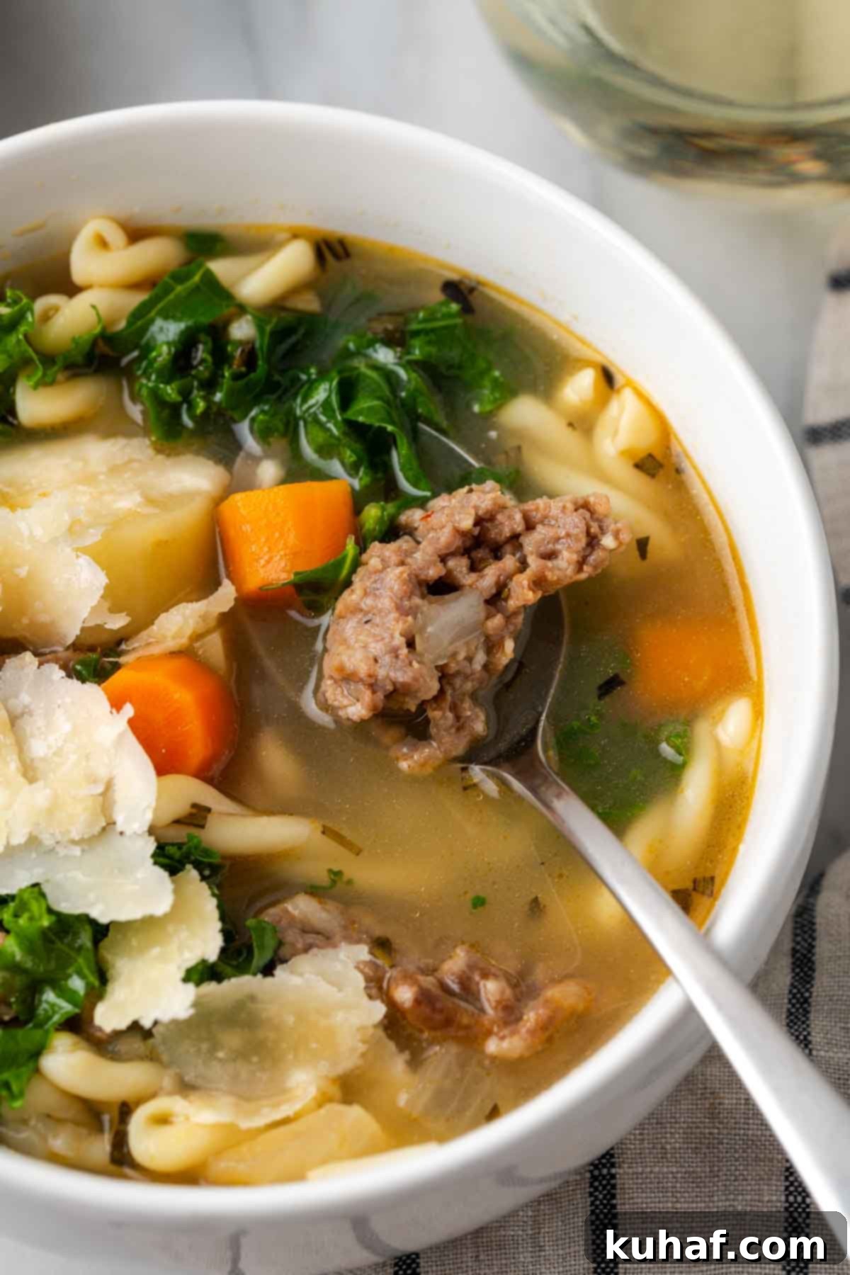 Italian sausage soup on spoon in white bowl.