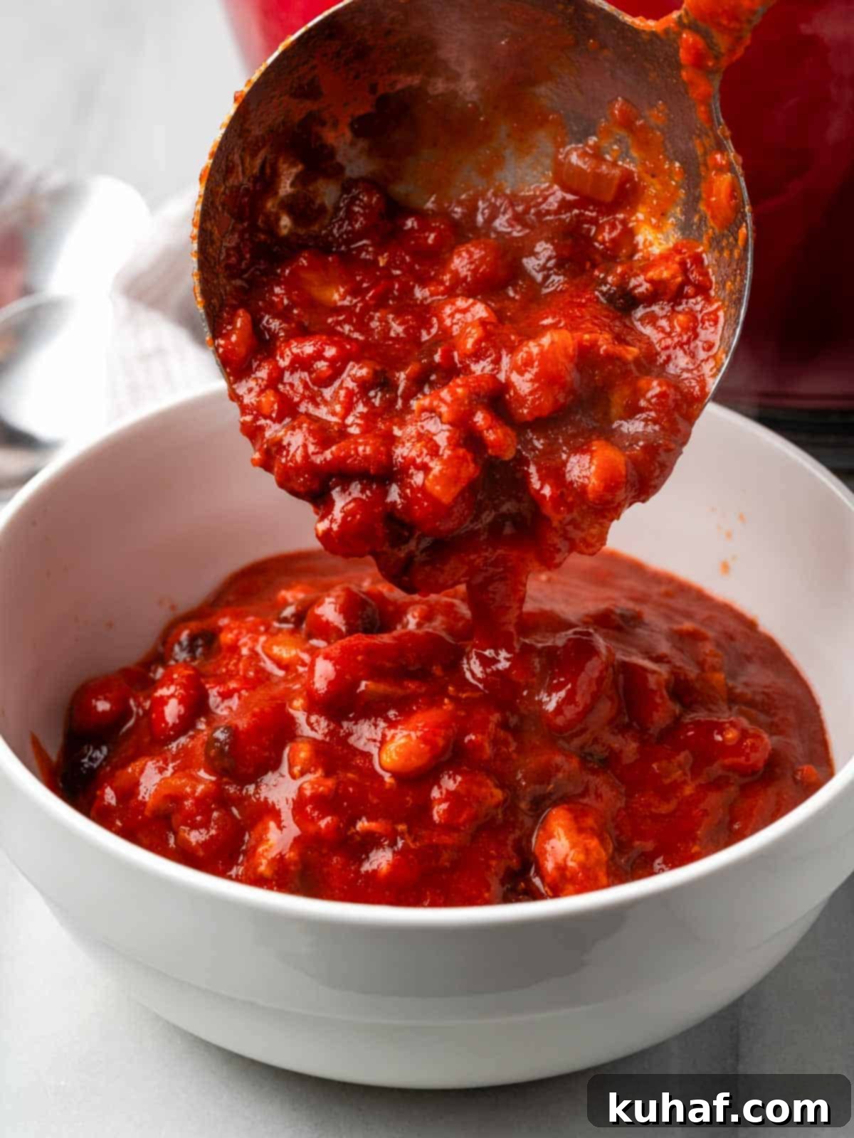 Pouring chili from a ladle into a bowl, showcasing its rich texture and color.