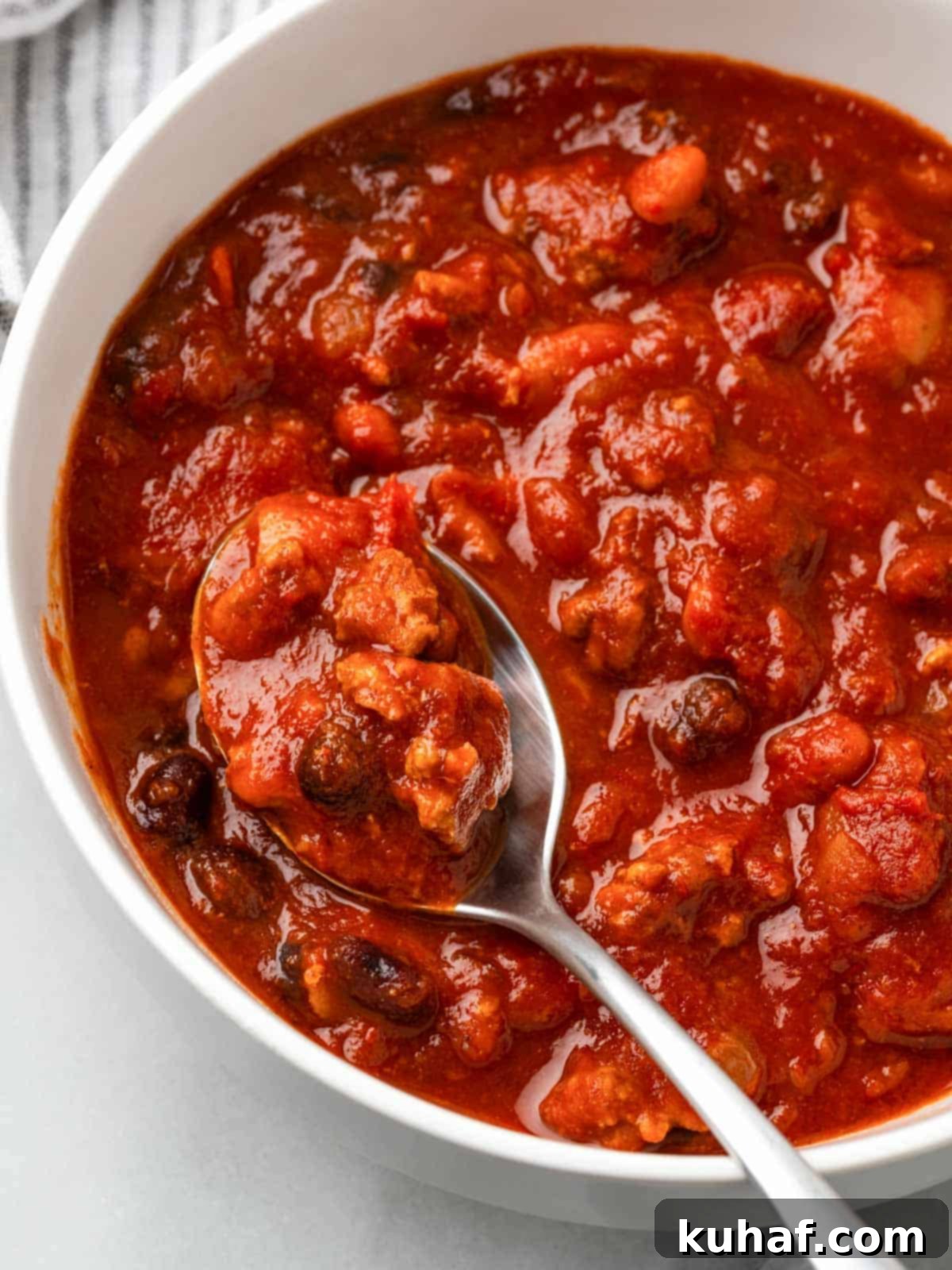 A spoonful of rich turkey chili held above a bowl, showing its chunky texture.