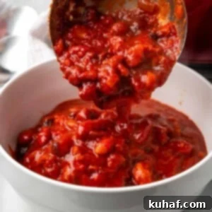 Serving chili with a ladle into a white bowl, ready for toppings.
