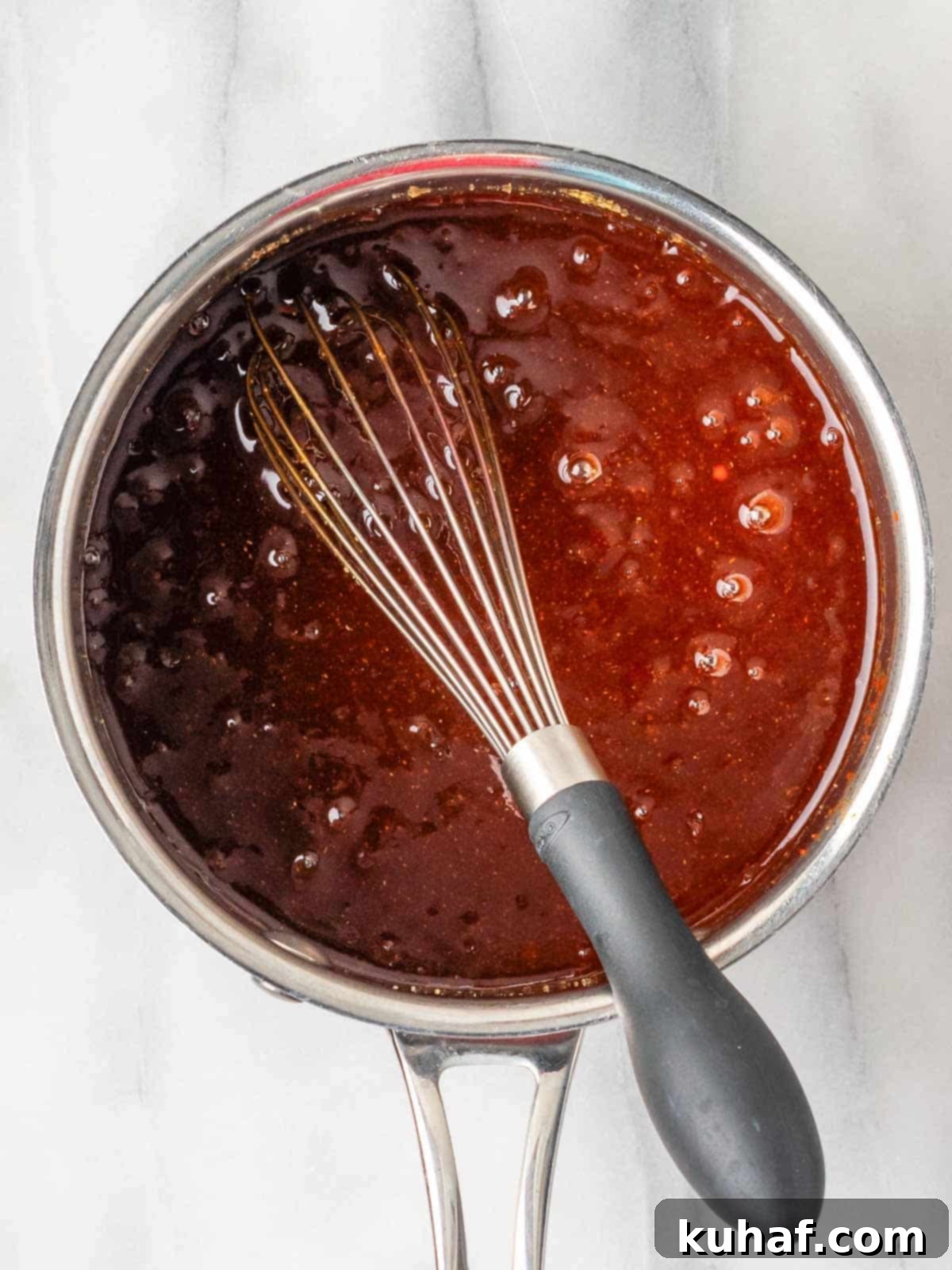 Homemade BBQ sauce simmering gently in a small pot with a whisk, showcasing its rich texture and inviting color, ready for any dish.