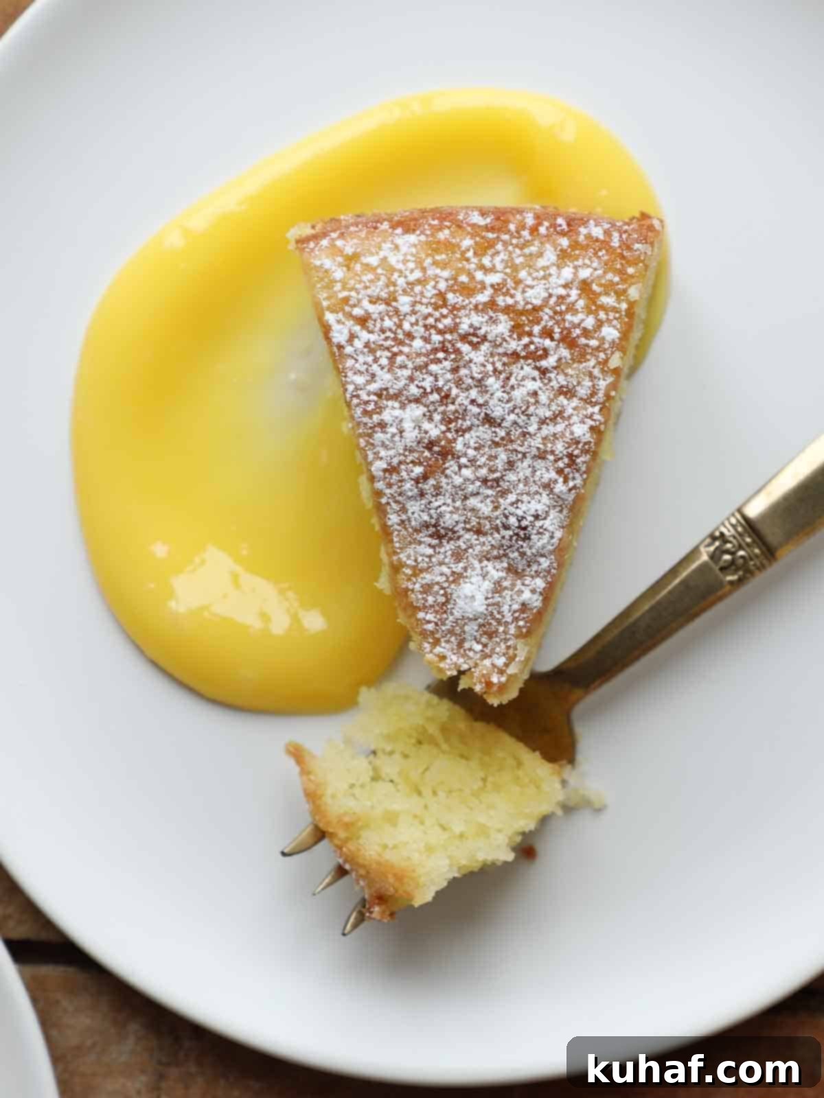powdered sugar on slice of olive oil cake on white plate with lemon curd.