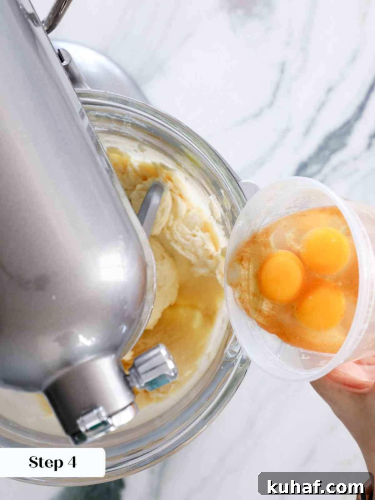 Adding eggs one by one to the vanilla cake batter during mixing.