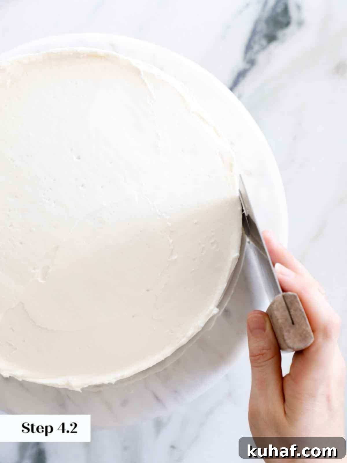 Smoothing the sides of a vanilla cake with a bench scraper for a clean finish.