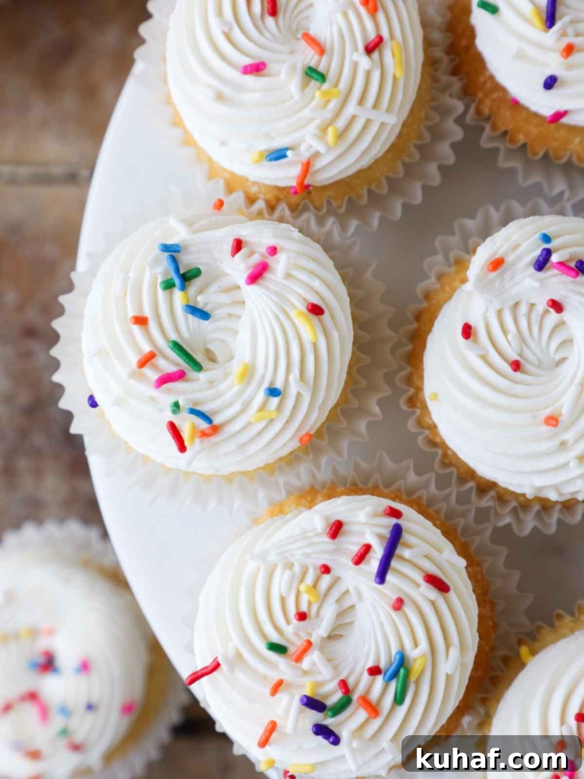 Vanilla cupcakes generously piped with fluffy ermine frosting and colorful sprinkles.