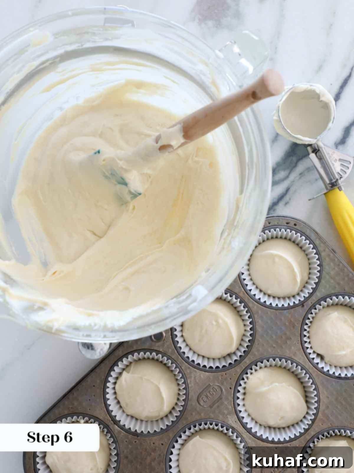 Chef portioning vanilla cake batter into cupcake liners using a cookie scoop.