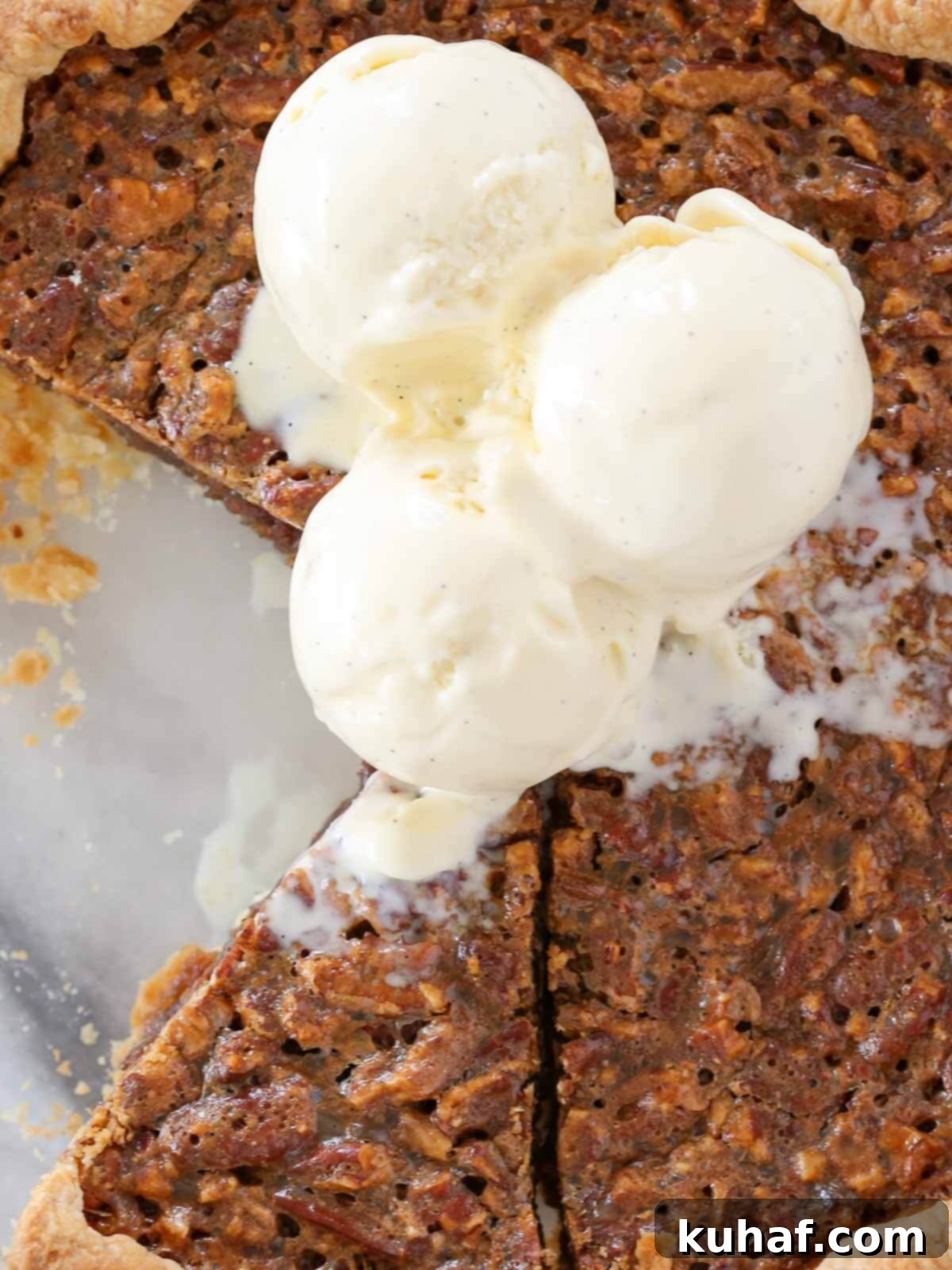 pecan pie sliced in dish with scoops of vanilla bean ice cream on top.
