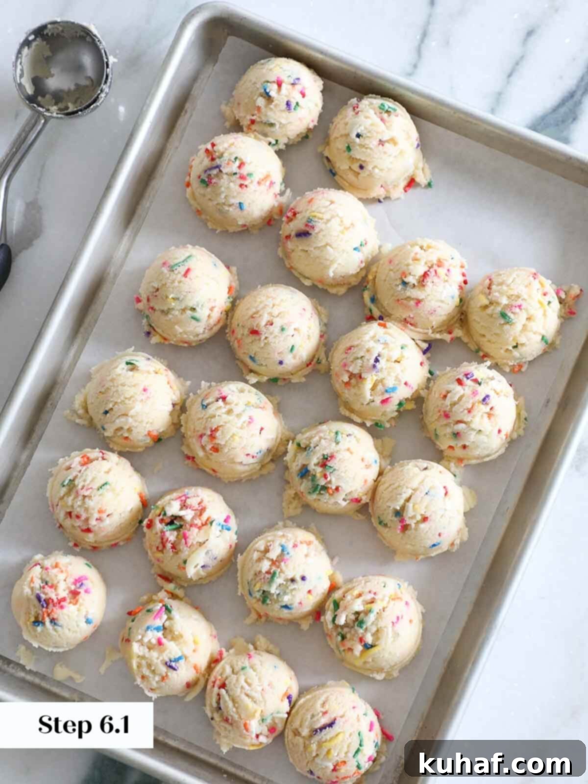 Funfetti cookie dough balls portioned and placed on a baking sheet, ready to be baked.