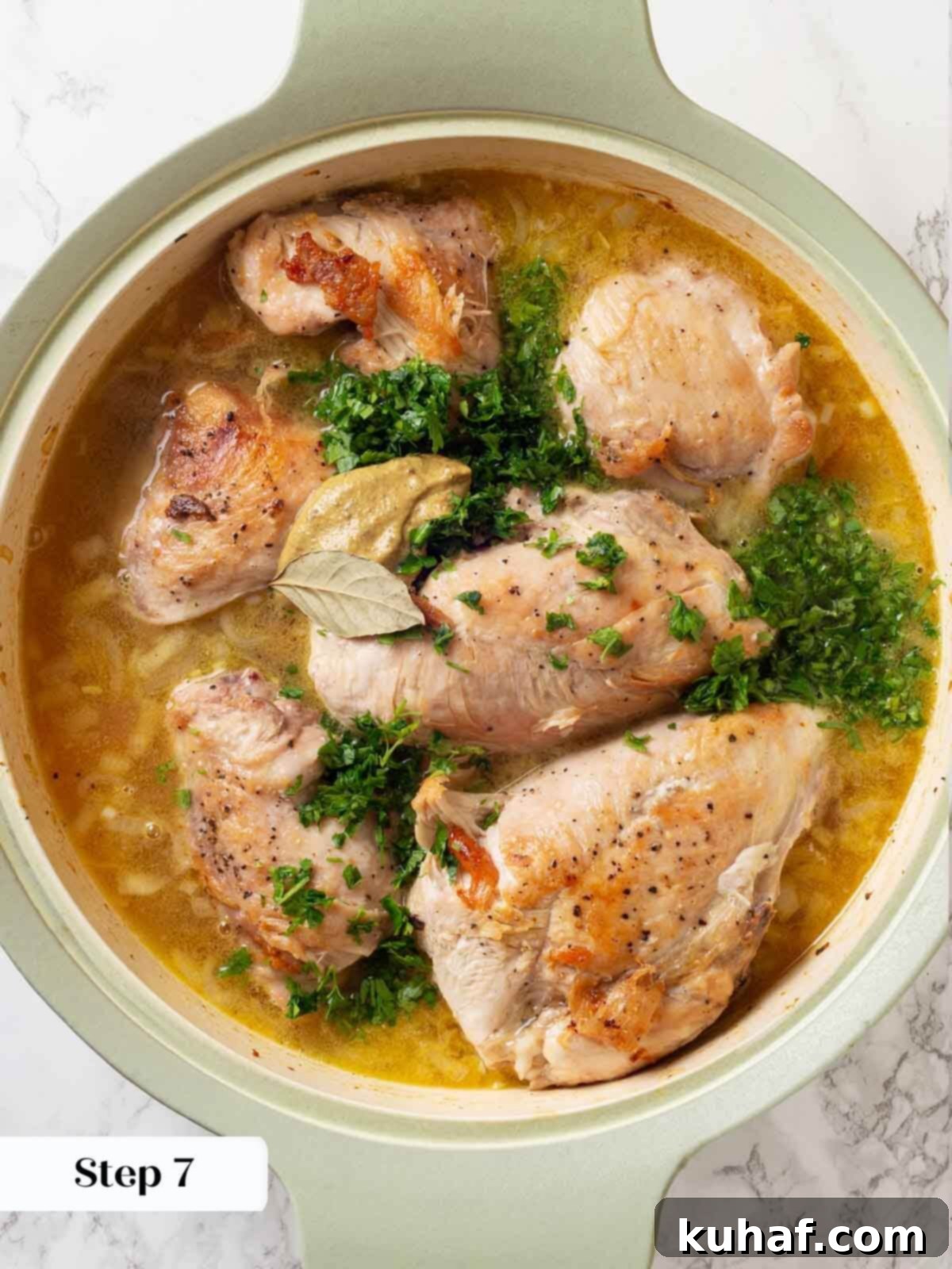 Chicken in wine sauce with a bay leaf added to the simmering liquid in a skillet.