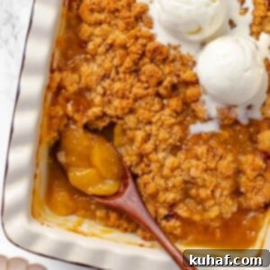 A wooden serving spoon scooping peach crisp from a dish.