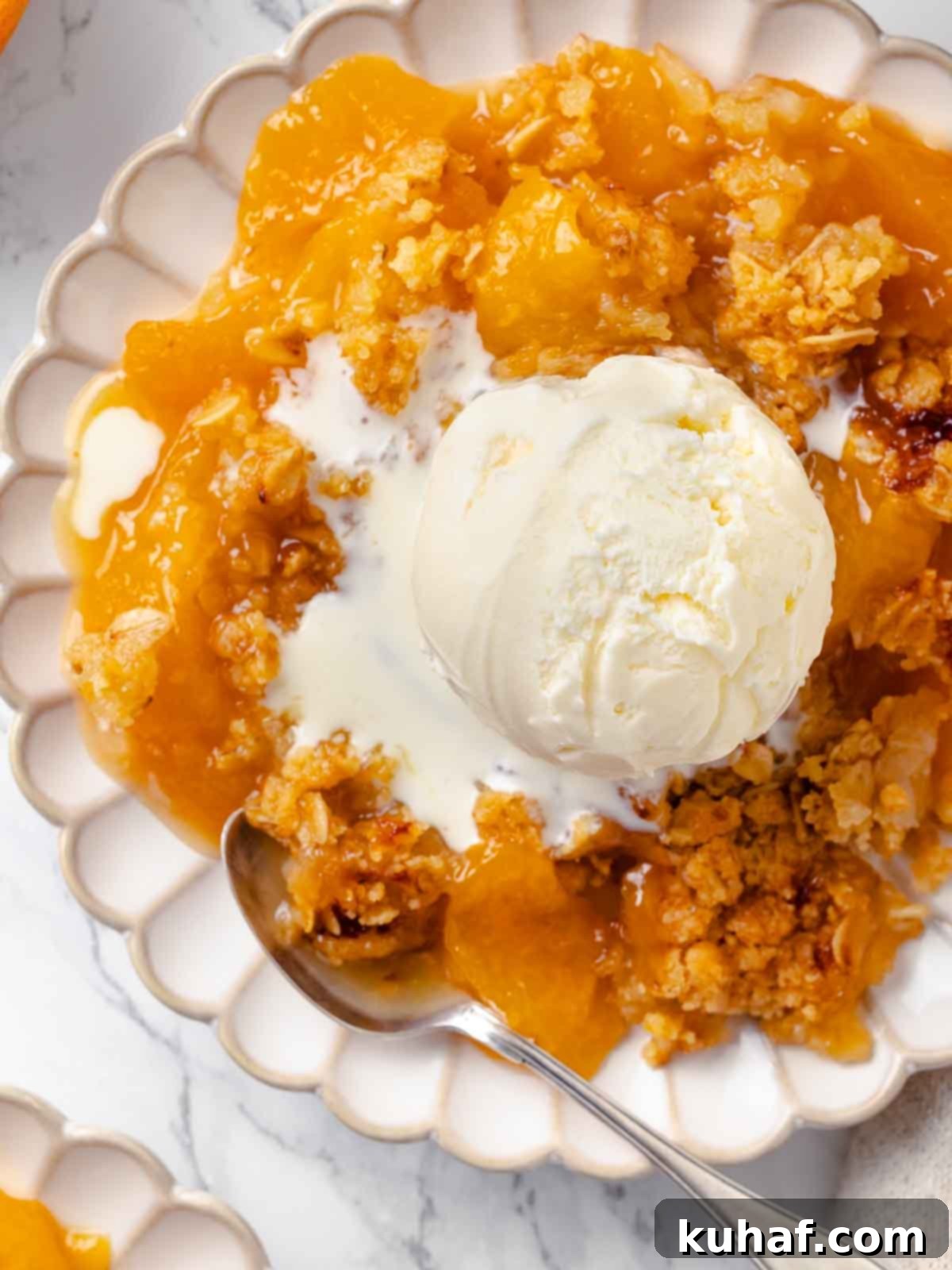 Peach crisp topped with melting vanilla ice cream, creating a creamy layer.