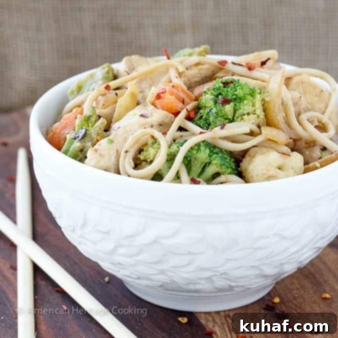A tantalizing overhead view of Thai Peanut Chicken Noodle Stir Fry in a hot skillet, showing the glossy, rich peanut sauce coating the chicken, udon noodles, and vibrant vegetables, ready to be tossed.
