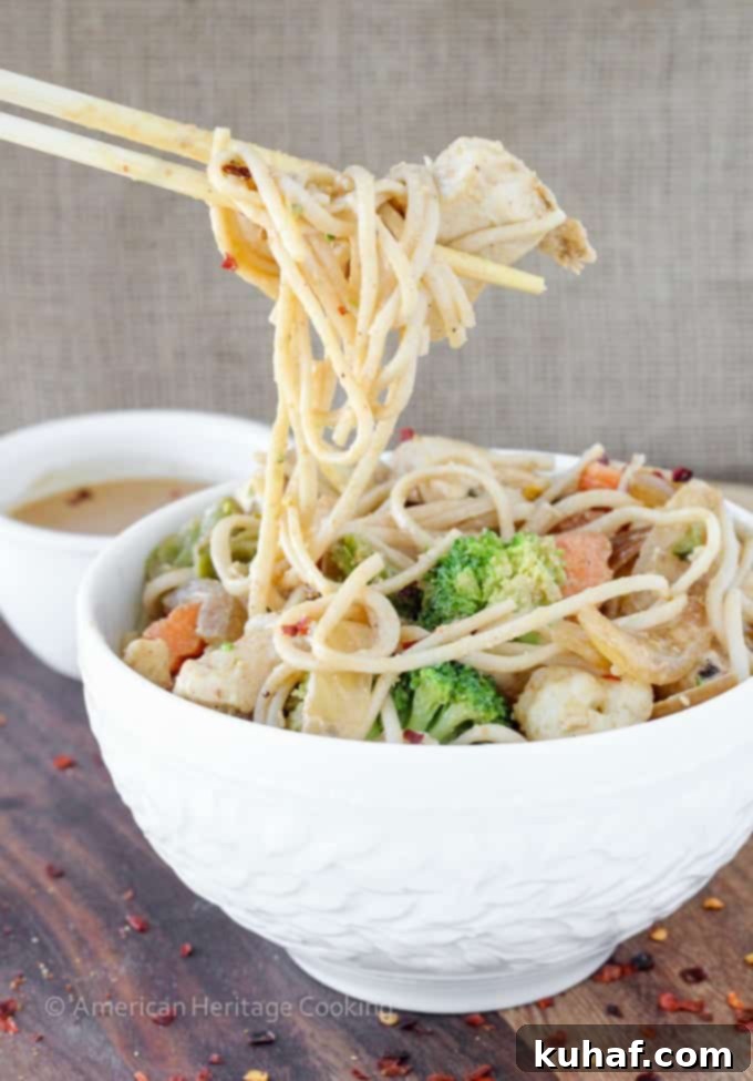A close-up shot of the Thai Peanut Chicken Noodle Stir Fry, highlighting the rich, glistening peanut sauce coating the udon noodles, tender chicken pieces, and brightly colored vegetables.