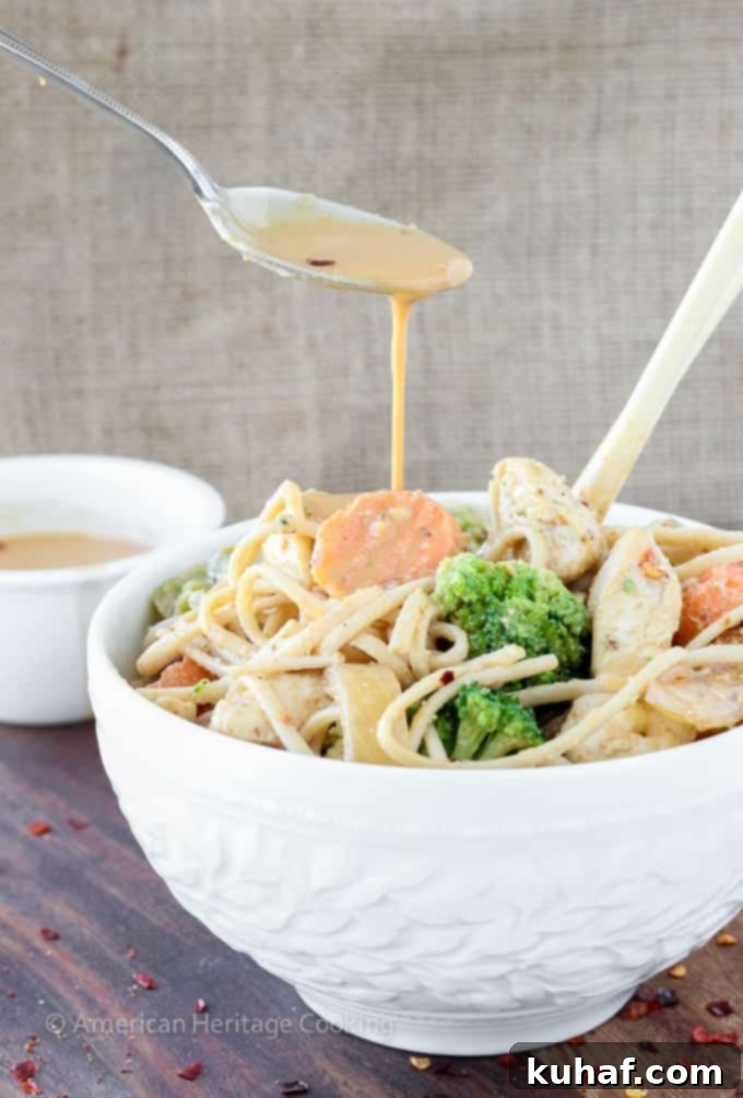 A beautifully arranged serving of Thai Peanut Chicken Noodle Stir Fry in a rustic bowl, showcasing the generous coating of rich peanut sauce on the chicken, udon noodles, and broccoli florets.