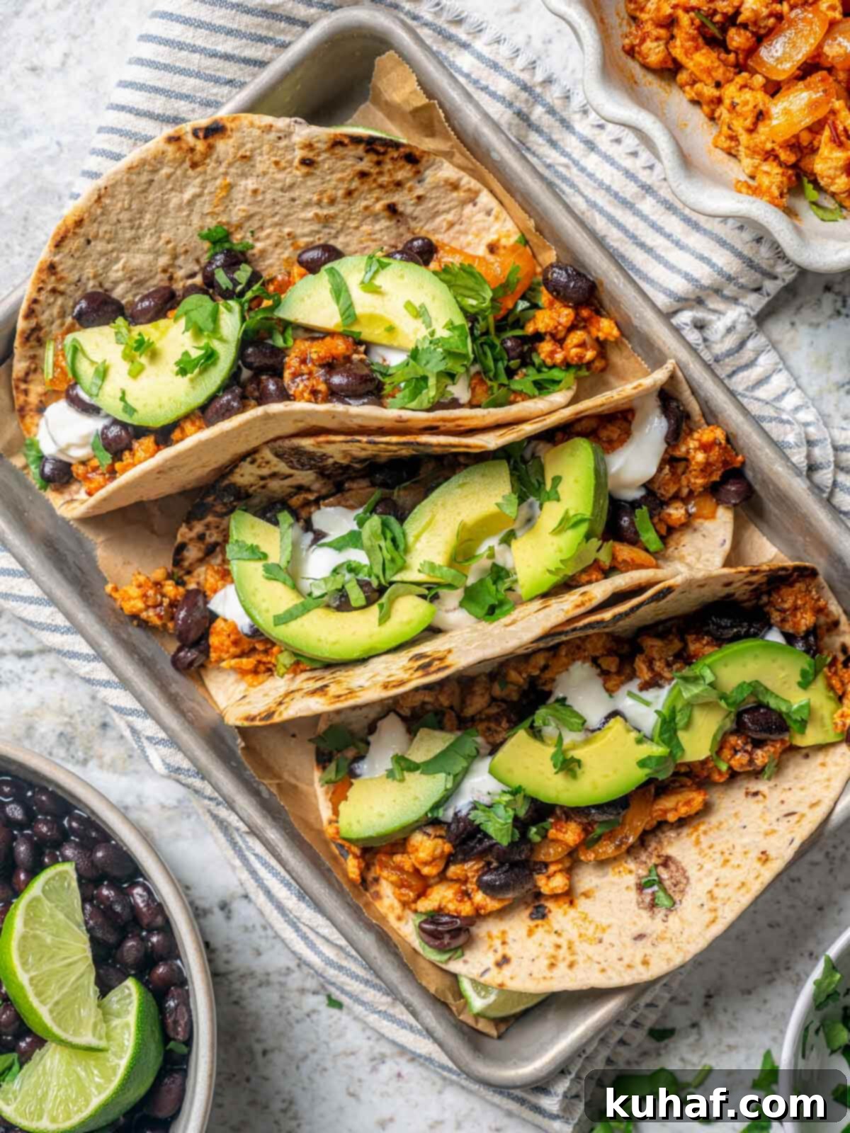 Three mouth-watering ground chicken tacos in whole wheat tortillas, topped with avocado, black beans, and cilantro, ready to eat. 
