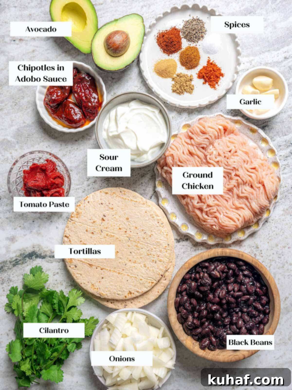 All the fresh ingredients for ground chicken tacos laid out on a marble surface, including chicken, onions, peppers, and spices.