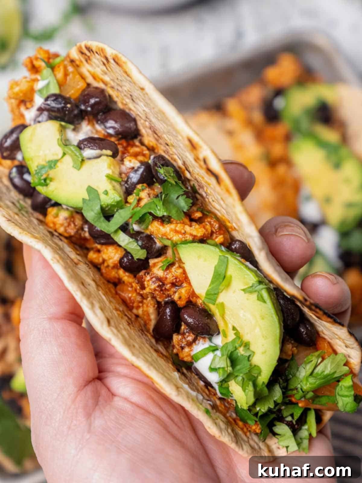 A hand holding a perfectly assembled ground chicken taco, showcasing its vibrant ingredients.