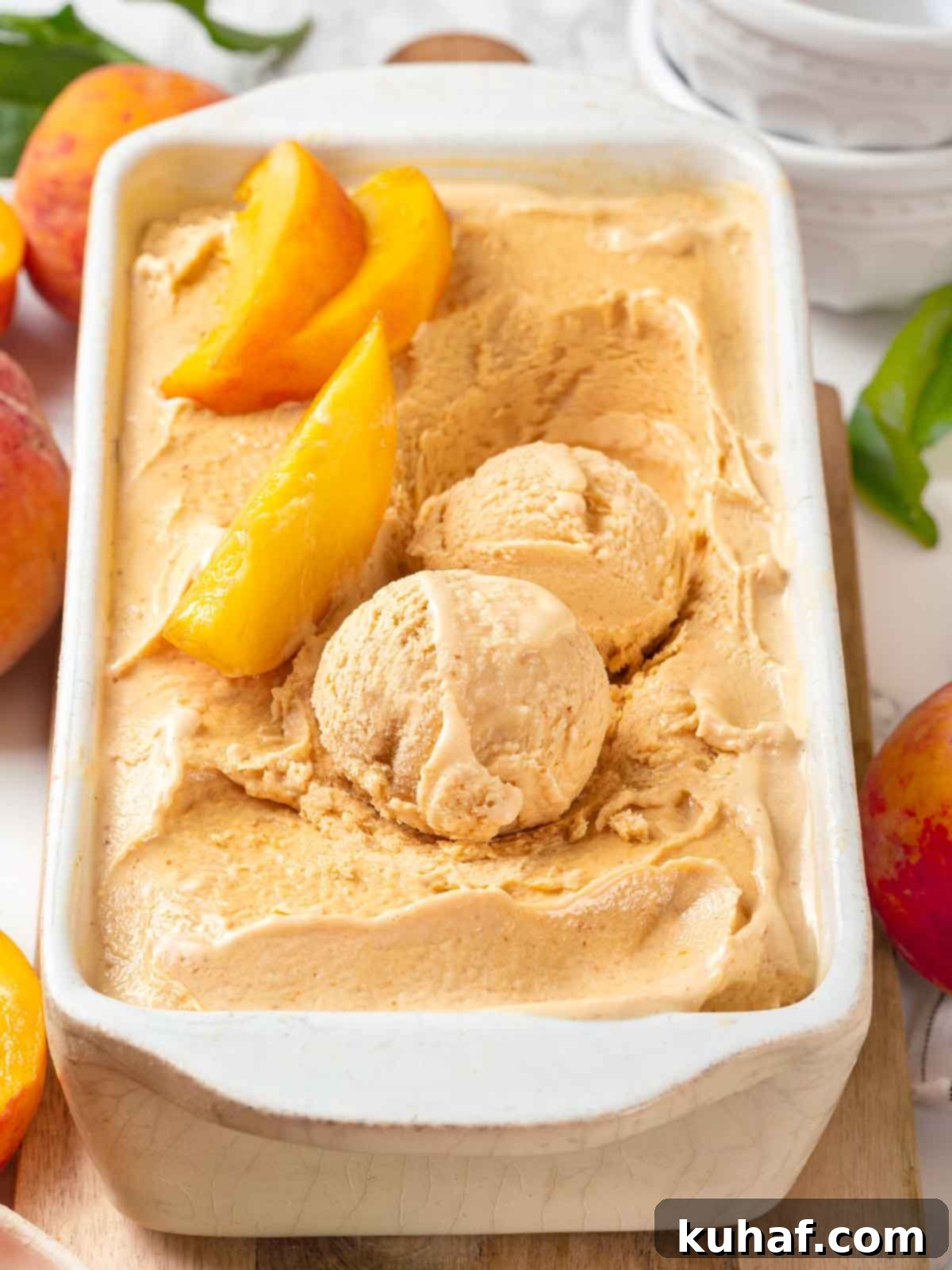 Scoops of creamy fresh peach ice cream in a white loaf pan, garnished with fresh peach slices.