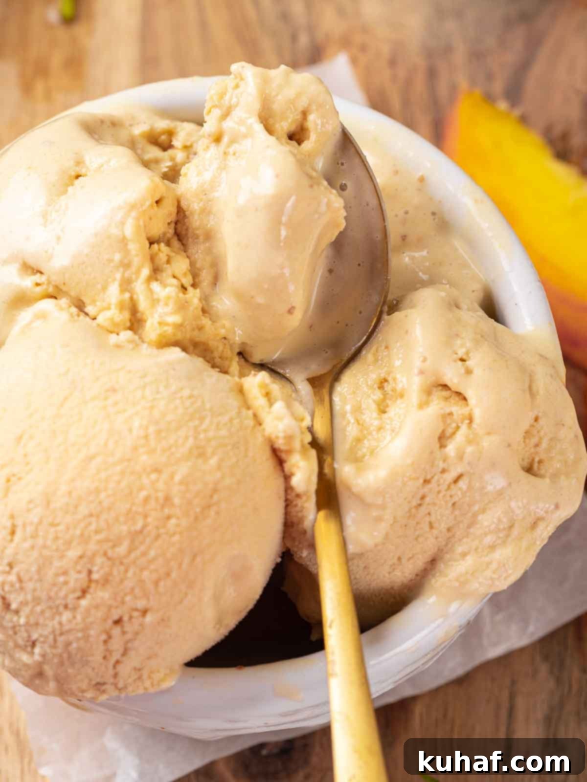 Three generous scoops of fresh peach ice cream in a white bowl, served with a golden spoon.