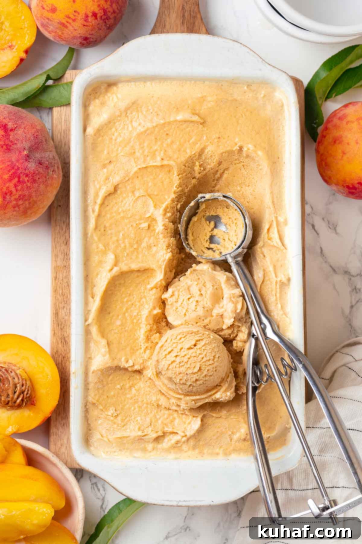 Generous scoops of fresh peach ice cream in a white loaf pan, accompanied by a vintage ice cream scoop, ready to serve.