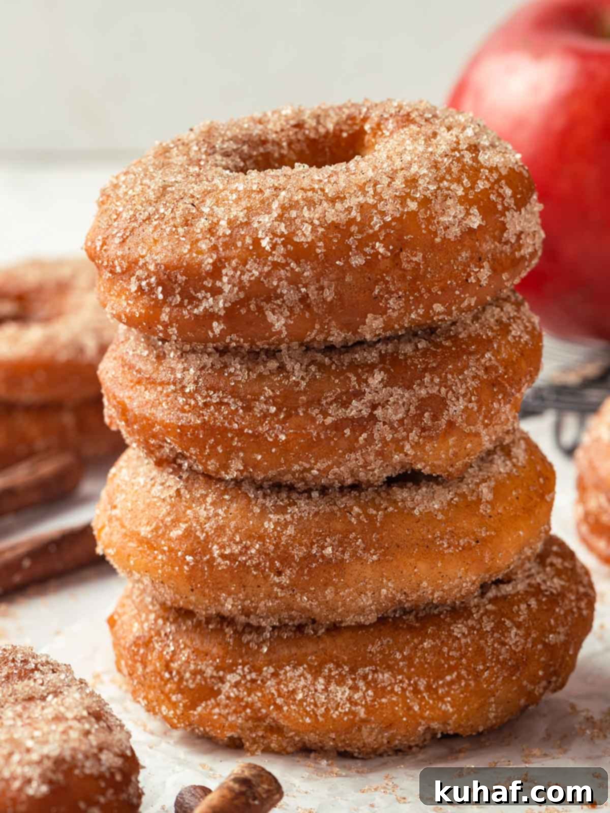 Four apple cider donuts stacked on top of each other, capturing their fluffy, sugary appearance.
