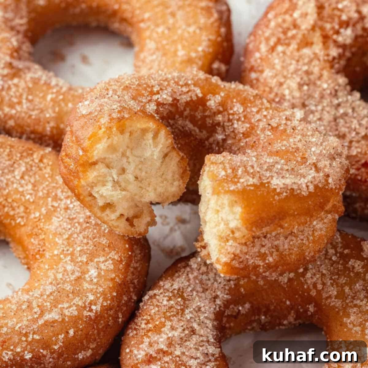 A set of apple cider donuts with the top one bitten, revealing the soft, airy interior.