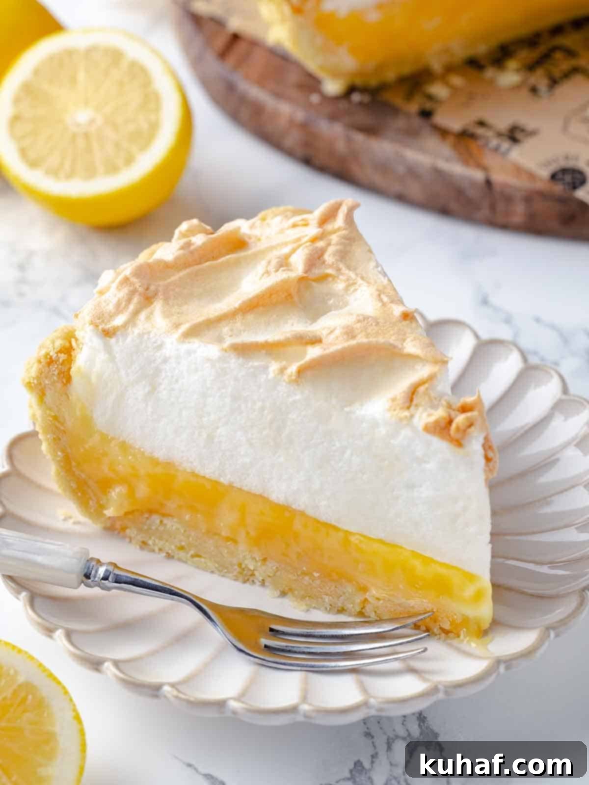 A slice of lemon meringue pie beautifully presented on a simple white plate, showcasing its golden meringue and bright yellow filling.