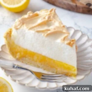 A slice of lemon meringue pie with a silver fork resting beside it, ready to be eaten, highlighting the beautiful texture and presentation.