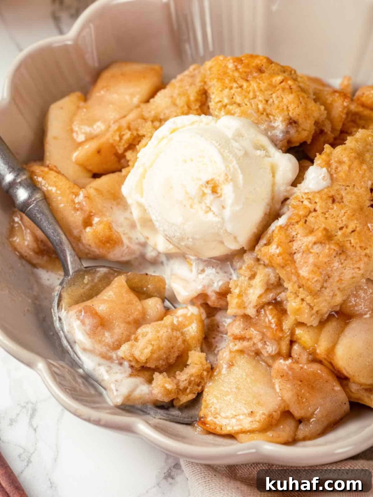 Apple cobbler in a white bowl, ready to enjoy, with a scoop of melting vanilla ice cream.