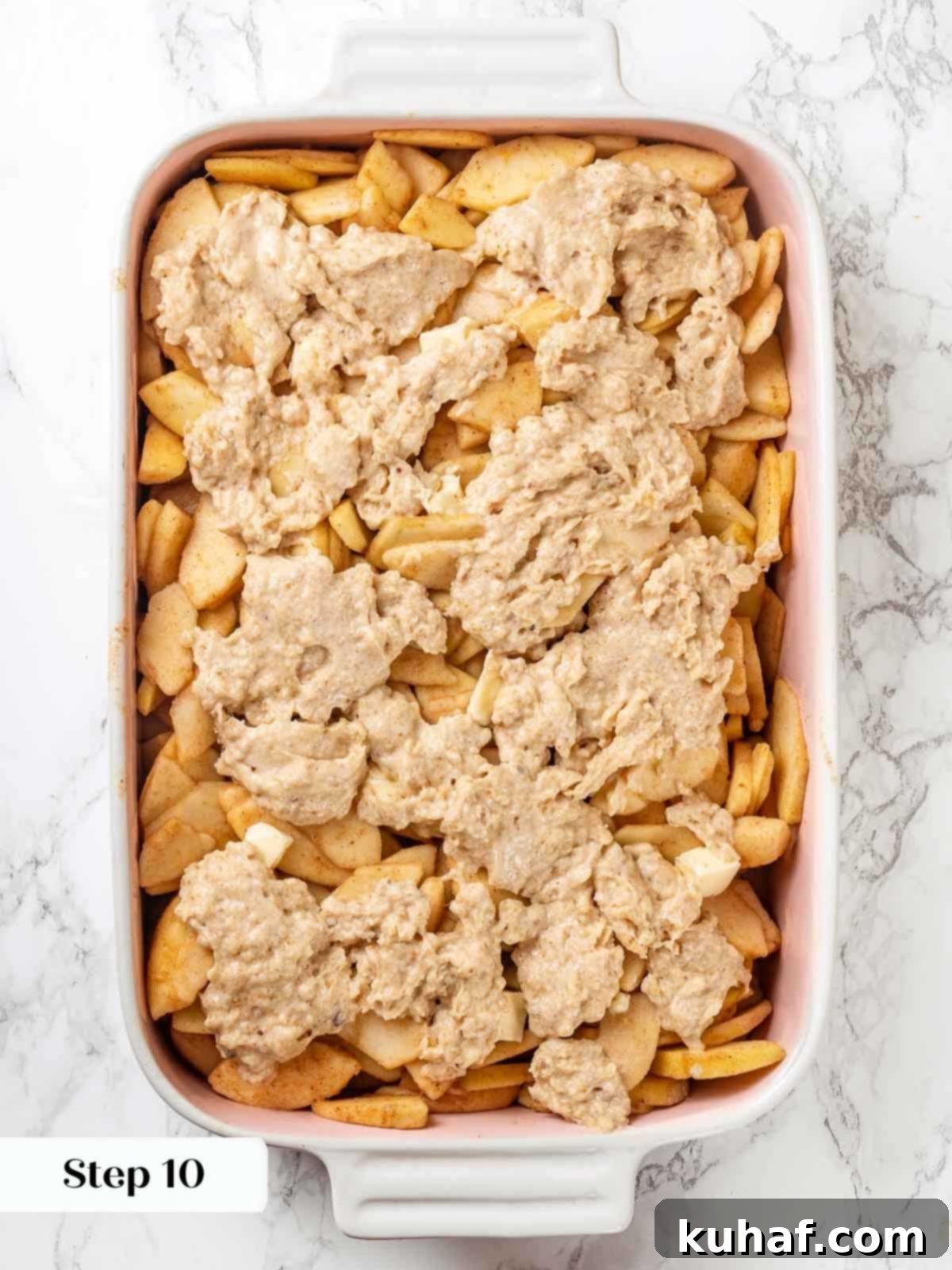 Unbaked apple cobbler, showing uncooked apple filling and biscuit topping in a baking dish.