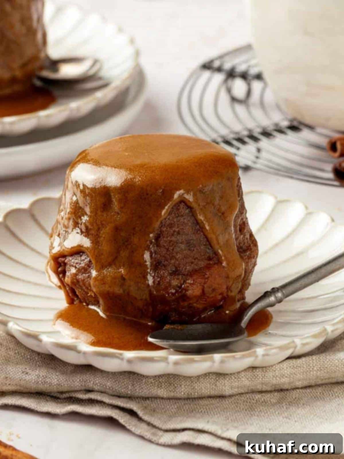 Sticky toffee pudding served on a white plate, topped with toffee sauce.