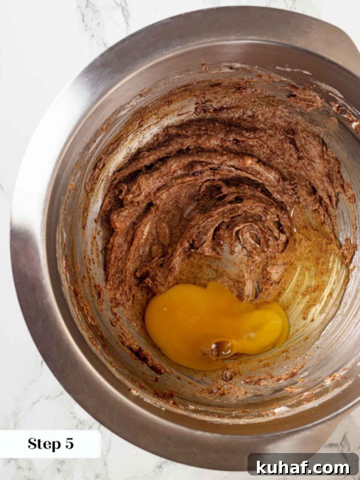 Eggs being added to sticky toffee pudding batter in a mixing bowl.