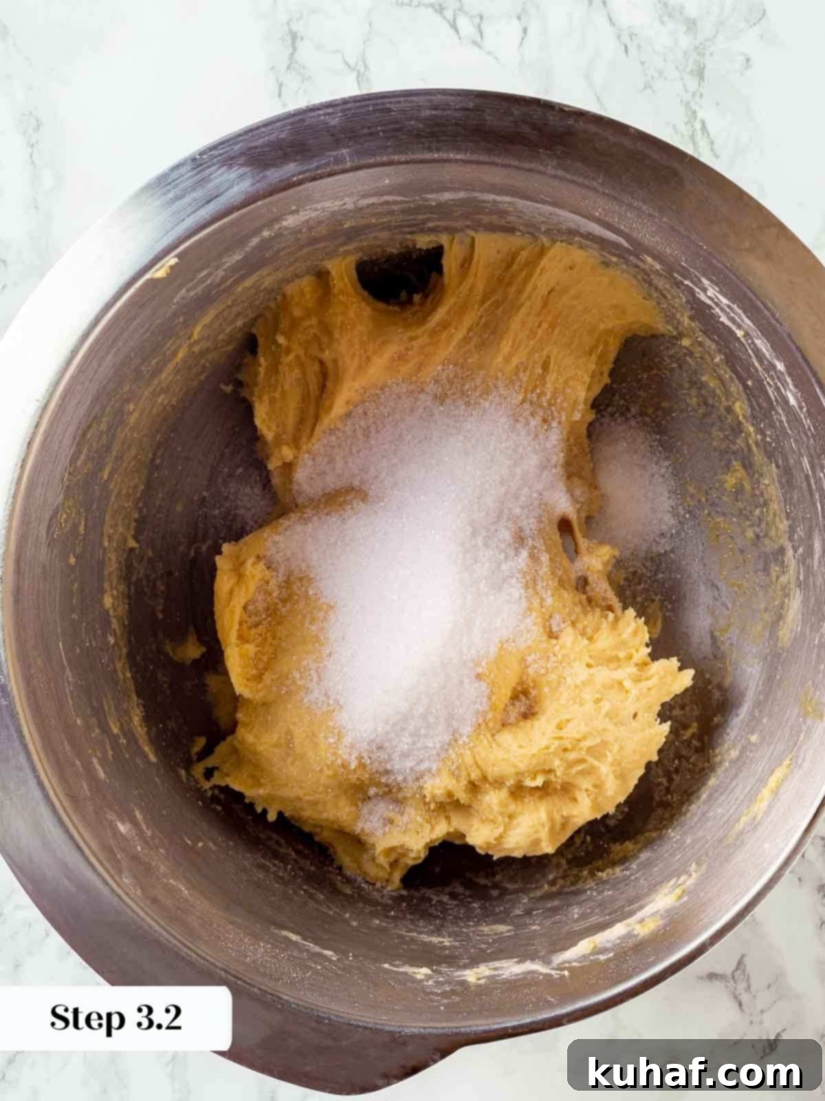 Granulated sugar being slowly added in batches to the panettone dough during mixing, ensuring even incorporation.