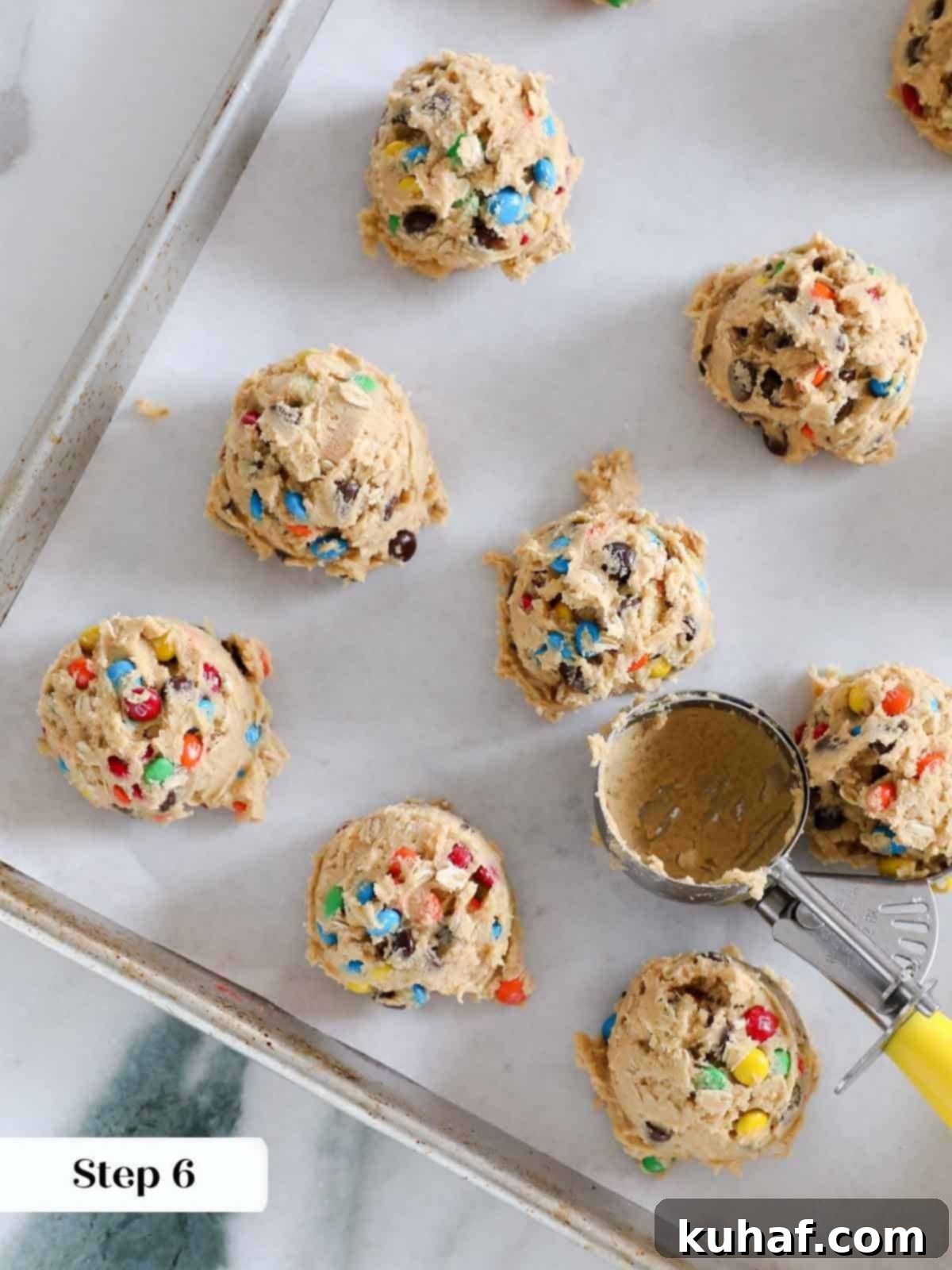 Perfectly scooped portions of monster cookie dough, uniformly spaced and ready for baking on a parchment-lined sheet.