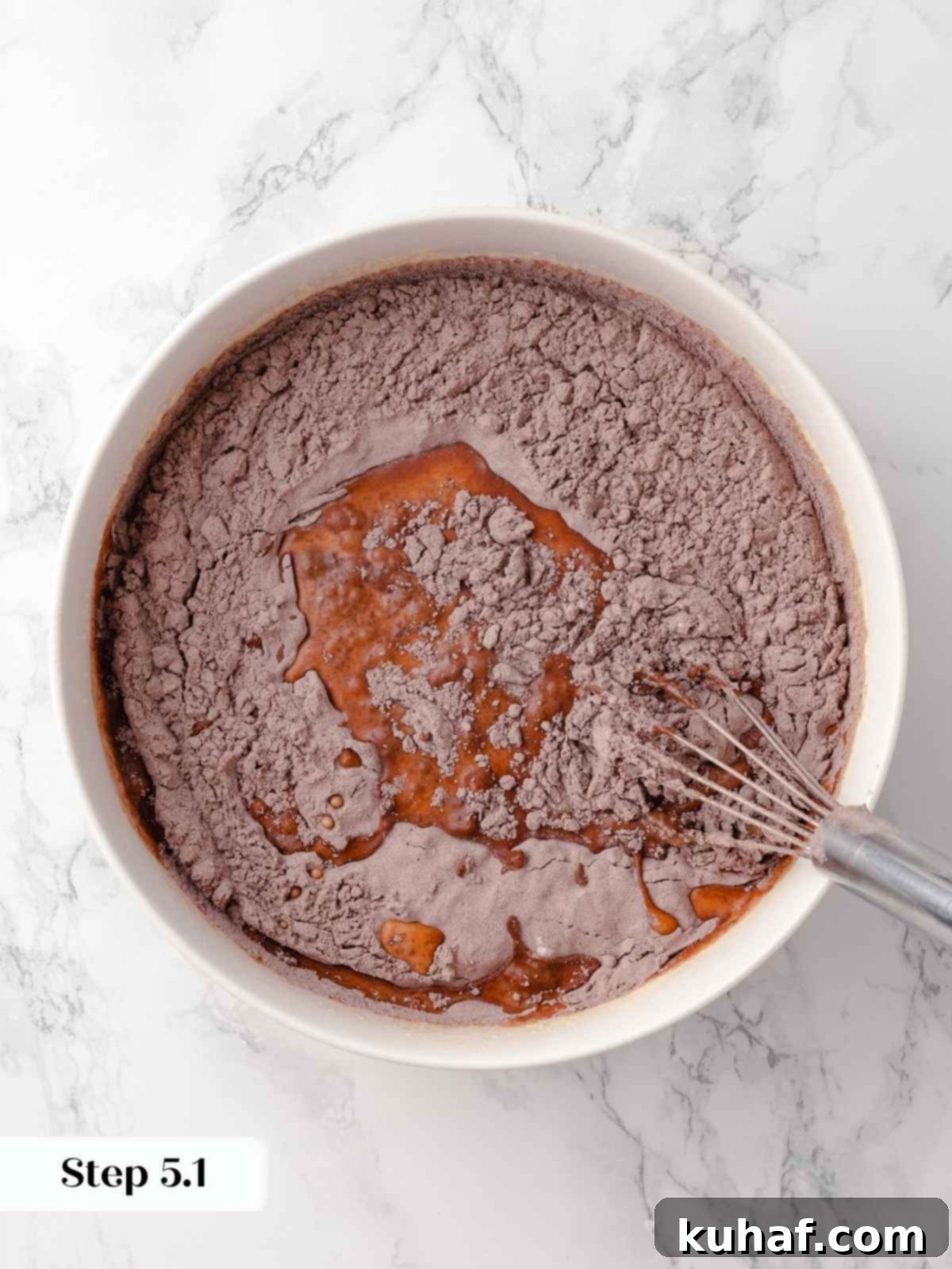 Dry ingredients being gradually added to wet ingredients in a mixing bowl for the chocolate cake batter, ensuring smooth integration.