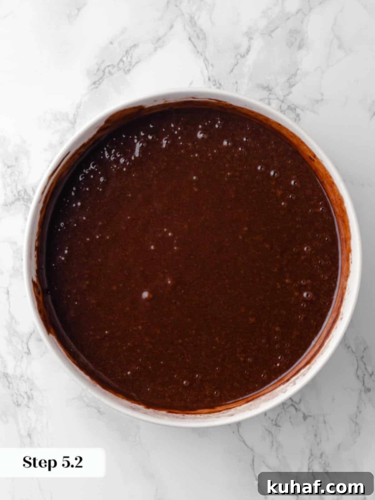 A mixing bowl filled with rich, glossy chocolate cake batter, perfectly smooth and ready to be poured into the cake pans.