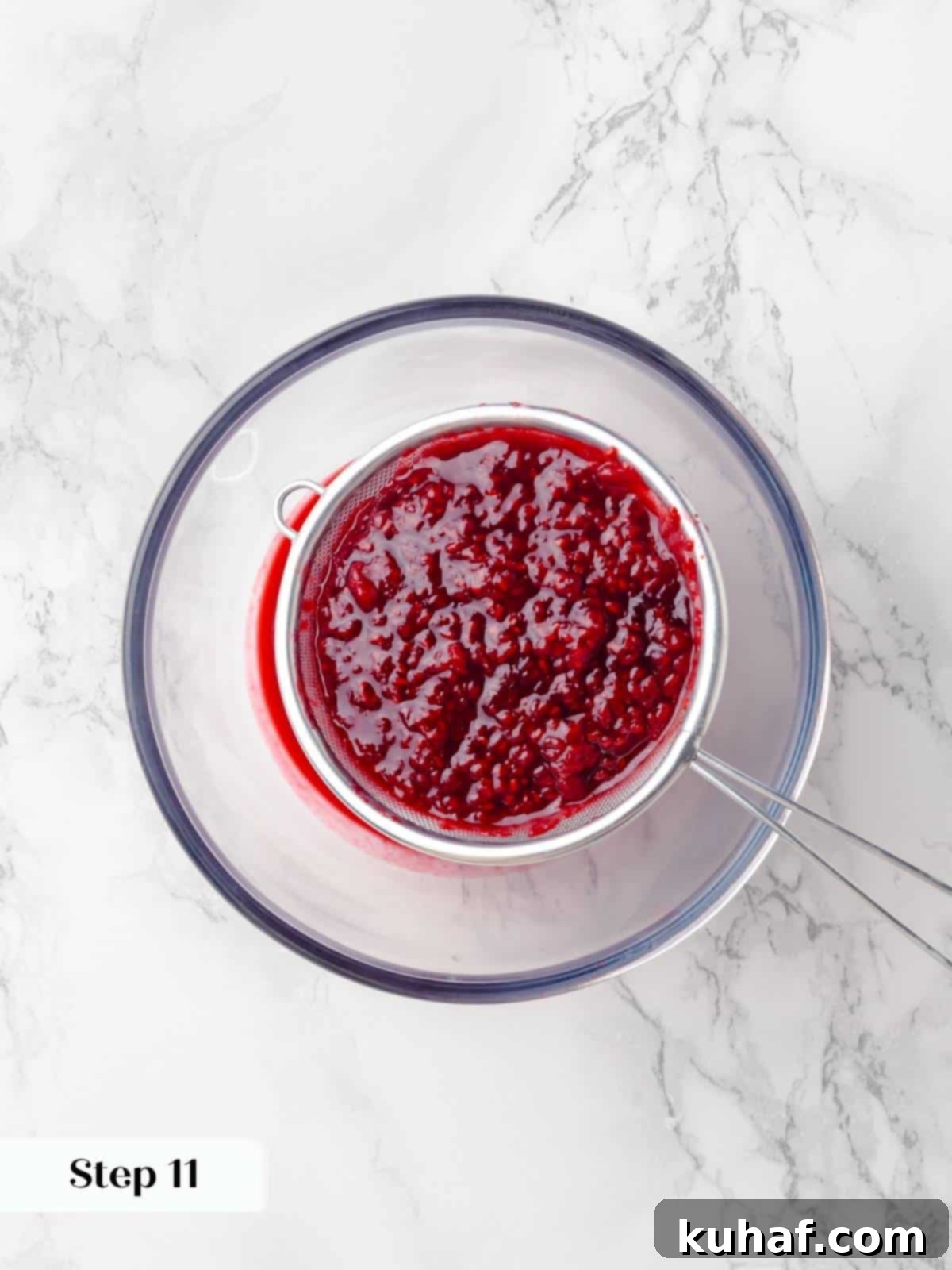 Fresh raspberries being strained through a fine-mesh sieve to remove seeds, ensuring a smooth jam for the chocolate raspberry cake.