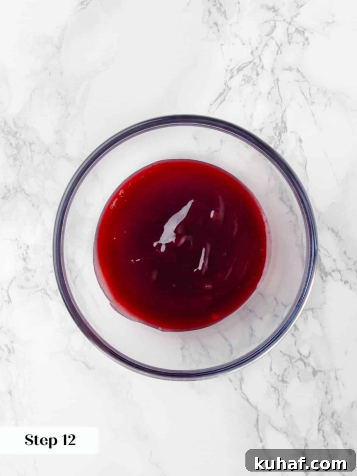 A clear glass bowl filled with vibrant, smooth raspberry jam, beautifully red and ready to be incorporated into the cake layers.