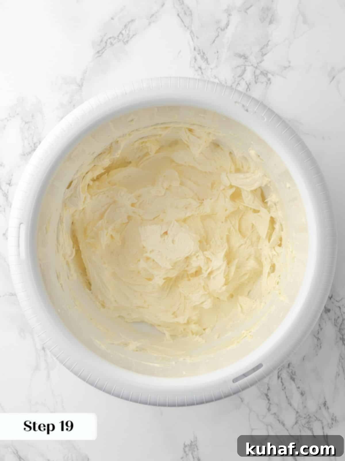 Butter being vigorously beaten in a stand mixer bowl, transforming into a light and fluffy base for the creamy buttercream frosting.