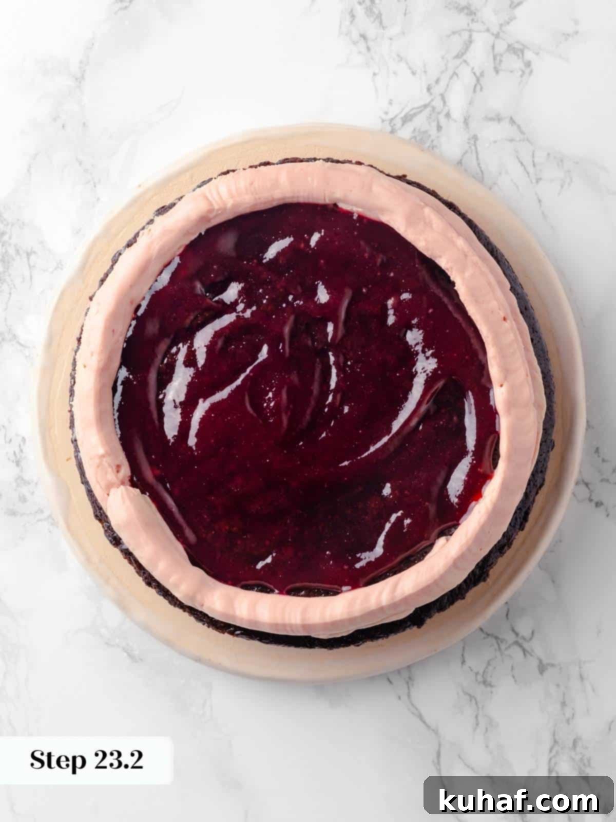 The first chocolate cake layer, generously topped with a bright raspberry jam filling and a piped ring of raspberry buttercream, prepared for the next layer.
