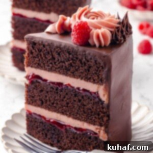 A stunning three-layer chocolate raspberry cake slice, showcasing its beautiful layers of chocolate cake, raspberry jam, and buttercream.