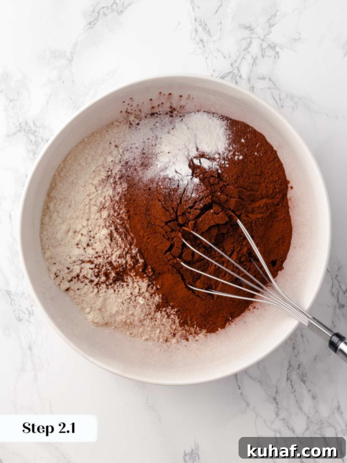 A bowl of dry ingredients being combined with a whisk for the chocolate raspberry cake batter, highlighting the dark cocoa powder.