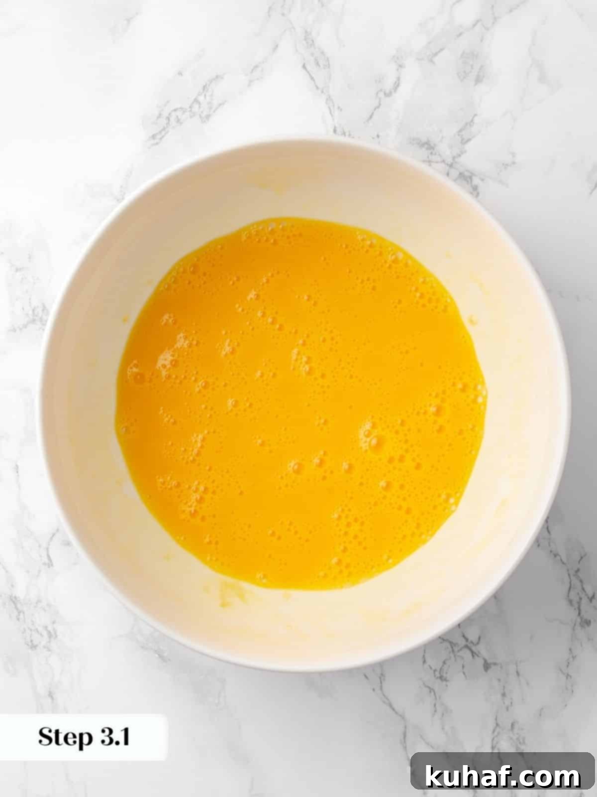 Eggs being vigorously whisked with vanilla extract in a bowl, forming a smooth, golden base for the cake batter.