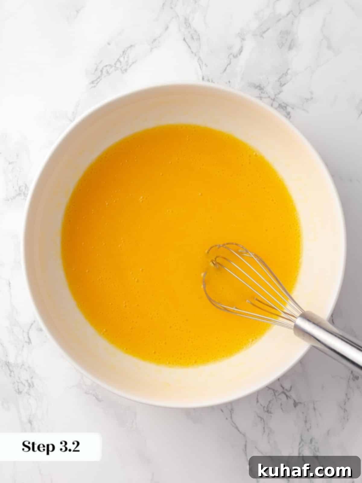 A whisk expertly mixing eggs with oil in a glass bowl, creating a perfectly emulsified and smooth cake batter base.