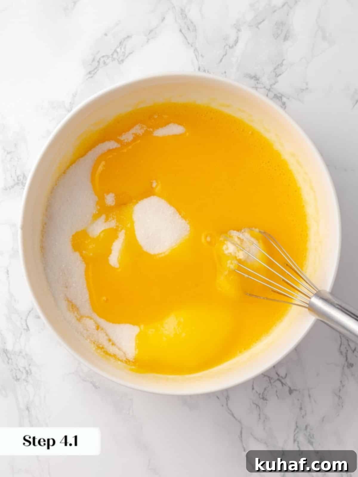 Granulated sugar being steadily added to whisked eggs in a clear glass mixing bowl, for the chocolate cake batter.