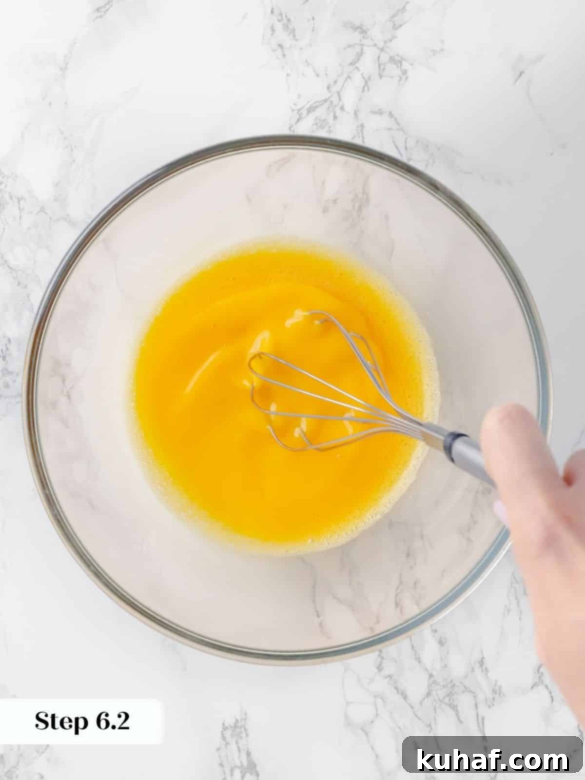 Eggs being thoroughly whisked in a mixing bowl until lightened and slightly increased in volume, forming a smooth base for the custard.