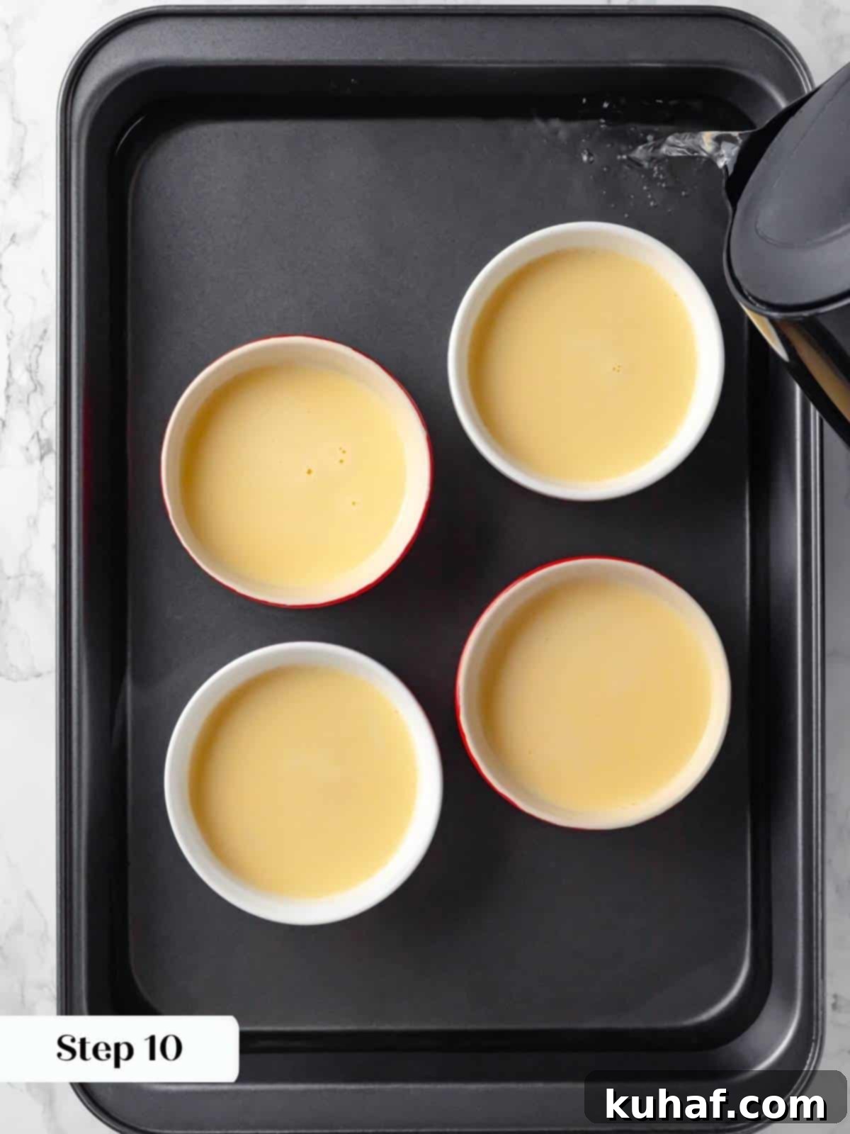 Hot water being carefully added to a baking pan, creating a water bath (bain-marie) for gentle baking of the crème caramel.